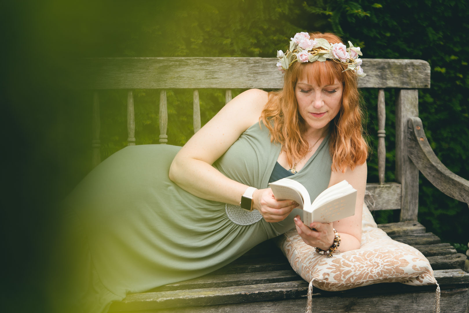 Portrait of Ginny Marsh wearing a green dress and flower crown, lying on a bench, reading a book. Branding shoot for Gorgeous You Retreats